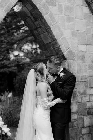 Romantic moment between newlyweds under a stone archway during their wedding day.