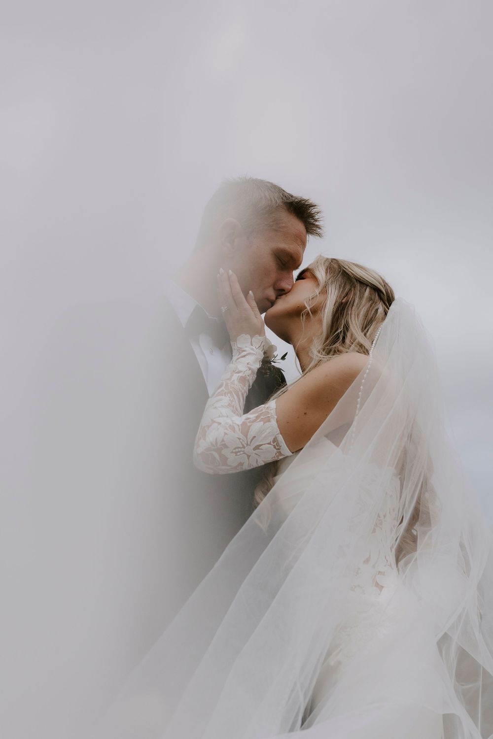 Ethereal bridal portrait with flowing veil against soft white background.