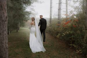 Newlyweds walking through a misty forest path with red autumn foliage.