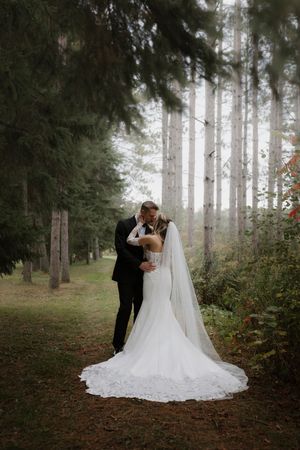 Wedding couple poses among tall pine trees in a romantic forest setting.