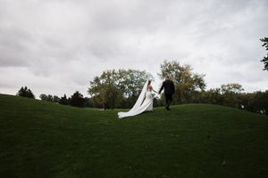 Wedding couple silhouetted against cloudy sky on rolling green hillside.