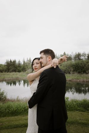 Romantic wedding portraits by a serene pond with evergreen trees in the background.