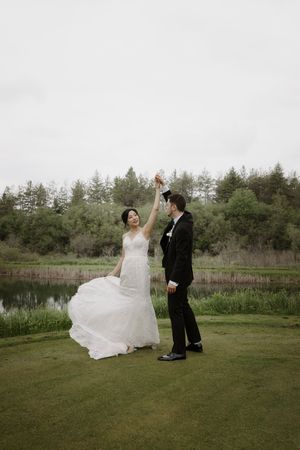 Newlyweds dance and twirl in an open field beside a tranquil pond.