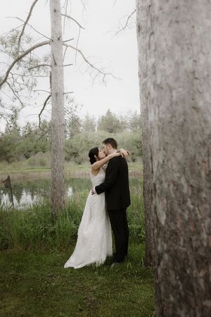 Wedding couple shares intimate moments between tall trees in a misty forest setting.