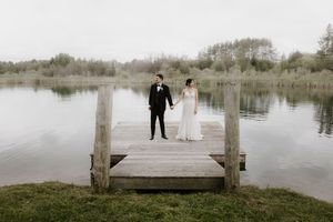 Wedding couple shares intimate moment on wooden dock overlooking serene lake and trees.