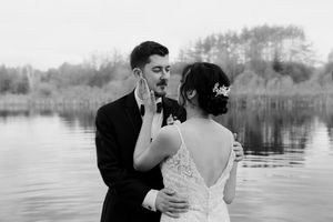 Romantic couple embraces on lakeside dock during overcast wedding day.