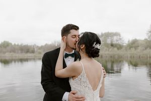 Newlyweds share tender moment on rustic wooden pier by tranquil water.