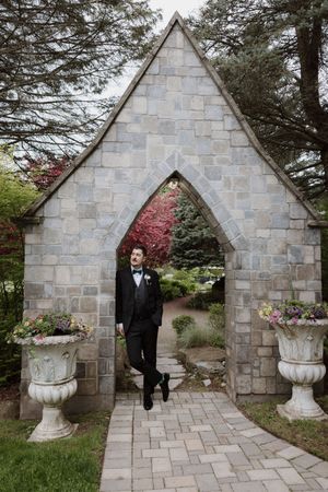 Stone chapel entrance with decorative urns and pink flowers creates romantic wedding backdrop.