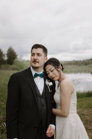 Wedding couple embraces by lakeside on overcast afternoon.