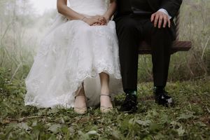 Wedding couple sits together on a wooden swing in an ethereal forest setting.