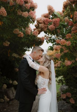 Romantic wedding moment under blooming pink hydrangea trees in garden setting.