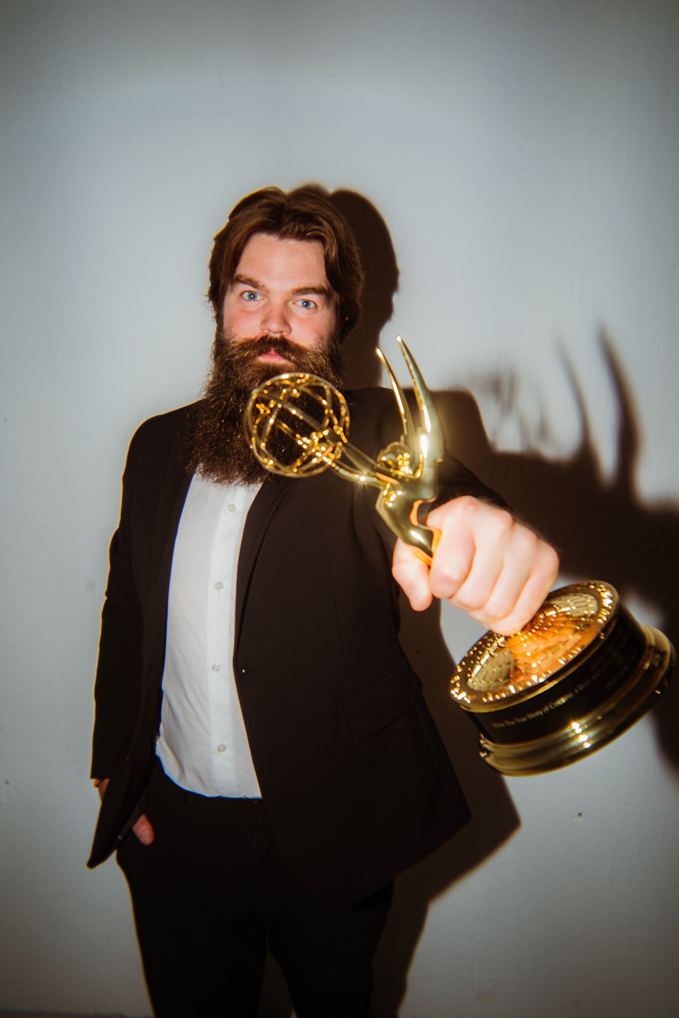 Person in formal attire holding up a golden Emmy award trophy against a light background.