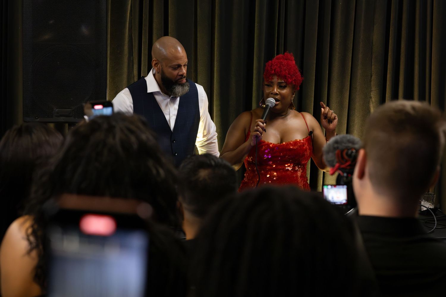 Performers entertain guests at an event with one wearing a sparkly red dress on stage.