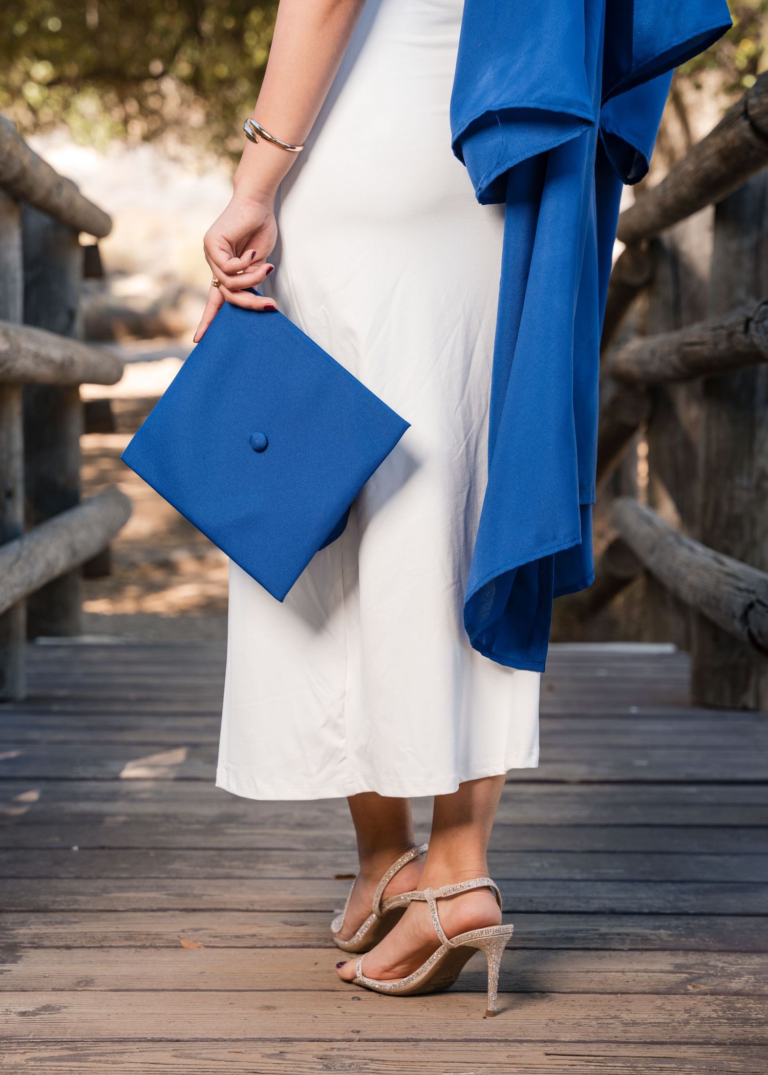 A person wearing a royal blue blazer and white dress walks across a wooden boardwalk showing their metallic heels.