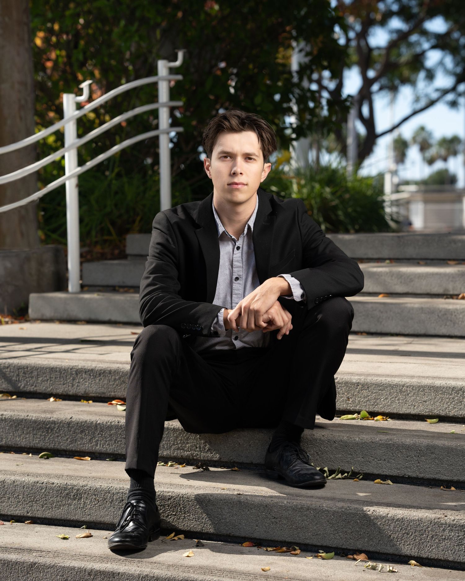 Professional portrait of person in dark suit sitting on concrete steps outdoors.