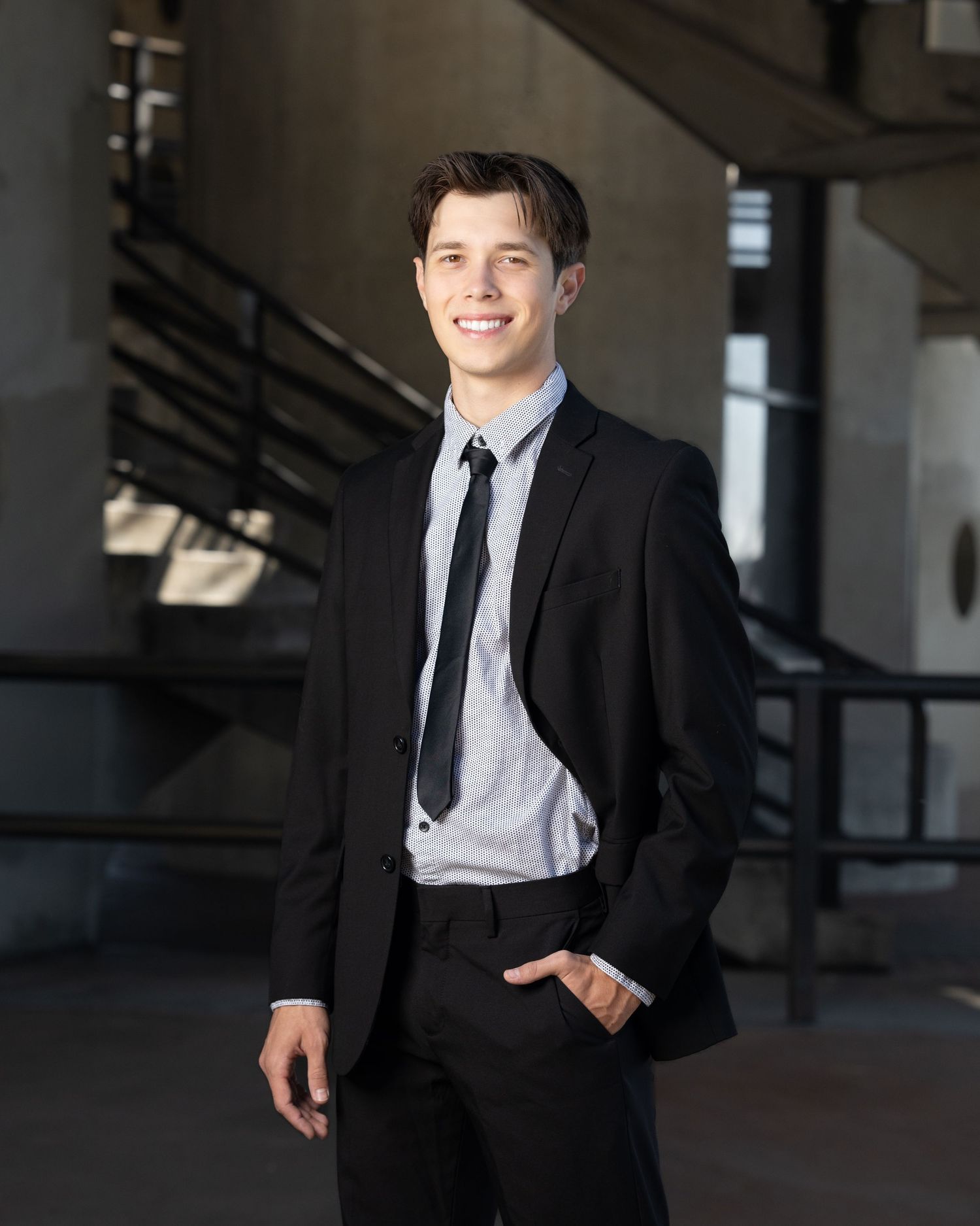 Business professional in black suit and tie standing in modern building interior.