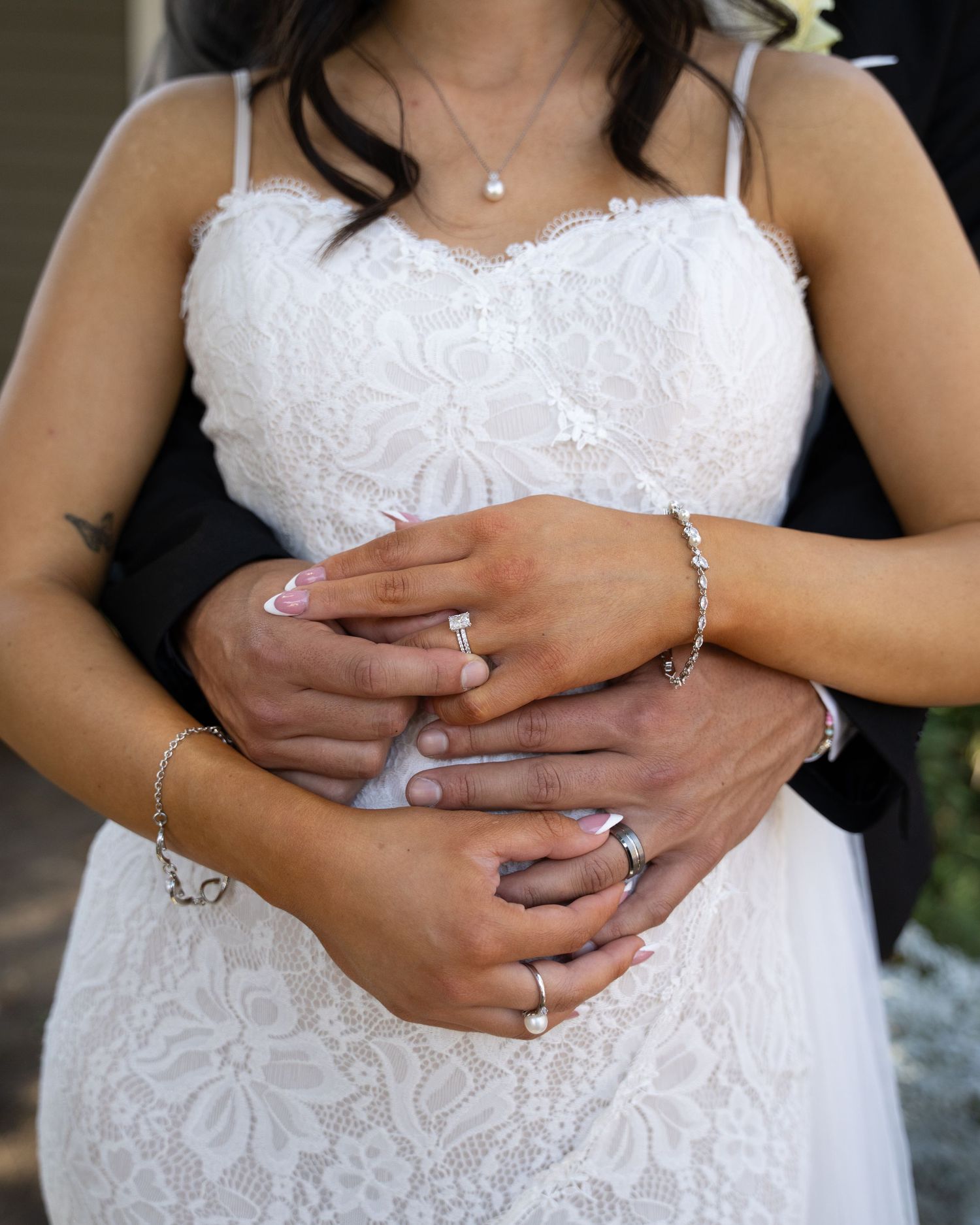Close-up shots of a bride's hands wearing an elegant wedding ring and bracelet against a white lace dress background.
