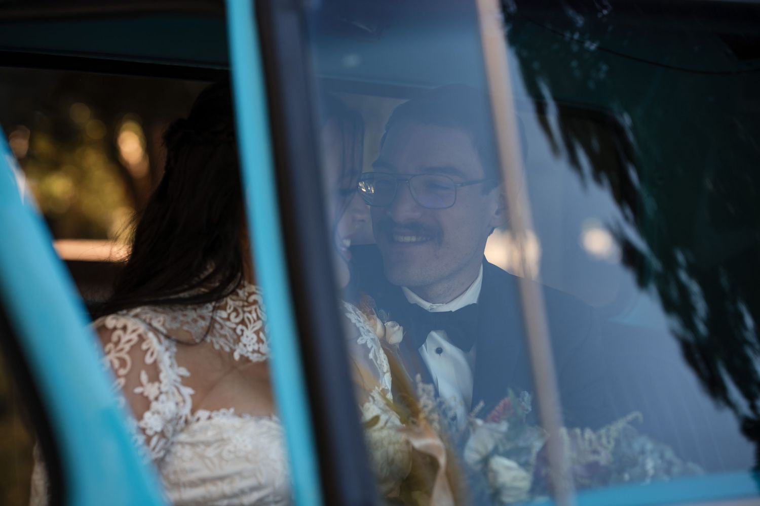 View through car window of newlyweds sharing a joyful moment during their wedding celebration.