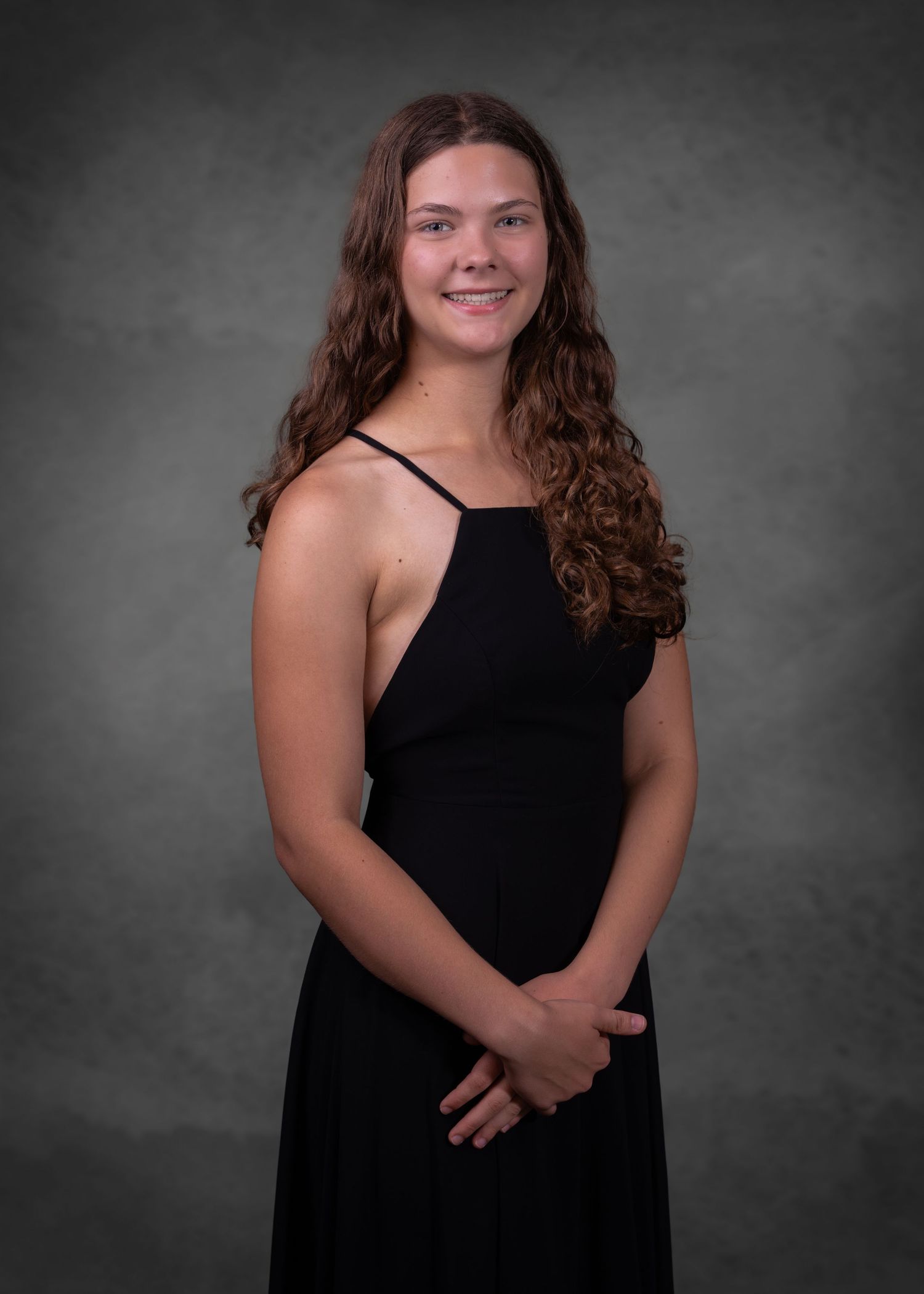 Young woman in black halter dress smiling for formal portrait photo against gray studio background.