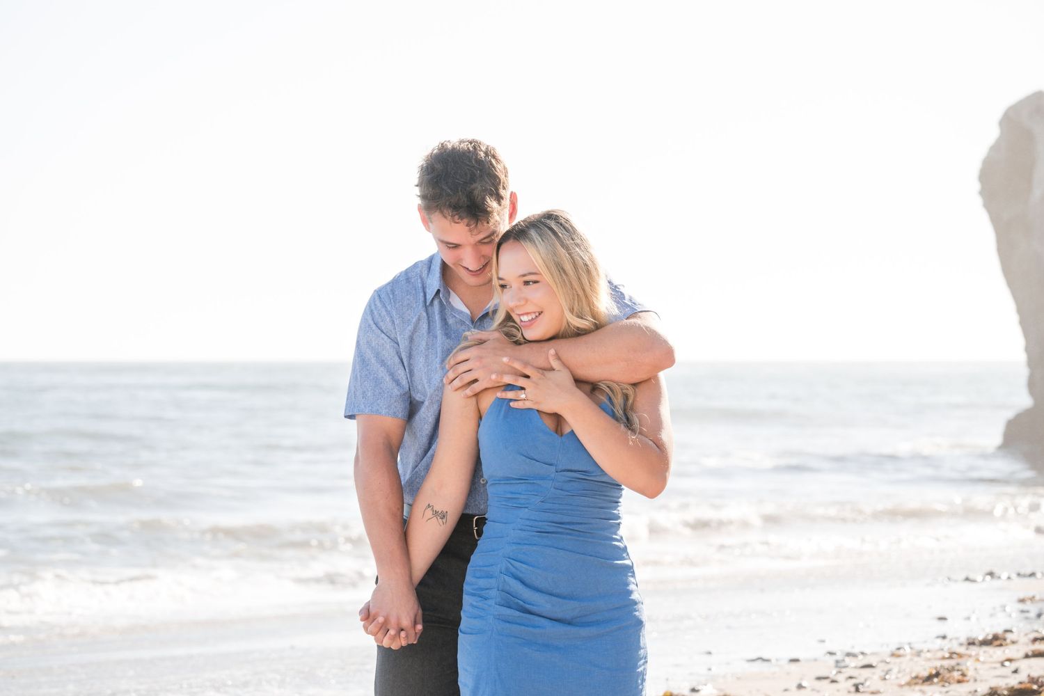 Romantic couple embracing on a sunny beach with cliffs in the background.