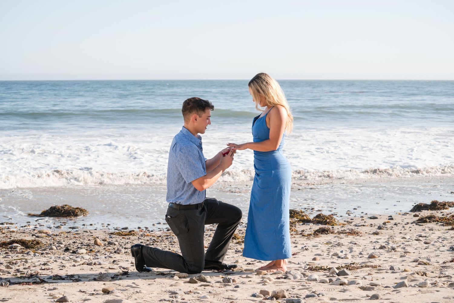 Beach proposal scene with ocean waves and rocky cliffs in the background.