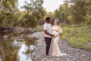 outdoor maternity session couple standing on rocky shoreline in front of bridge