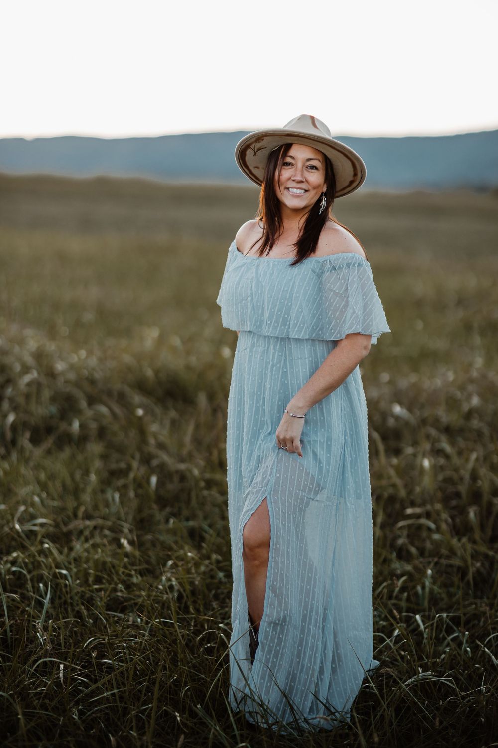 Light blue maxi dress and wide brim hat create dreamy silhouette in mountain field.