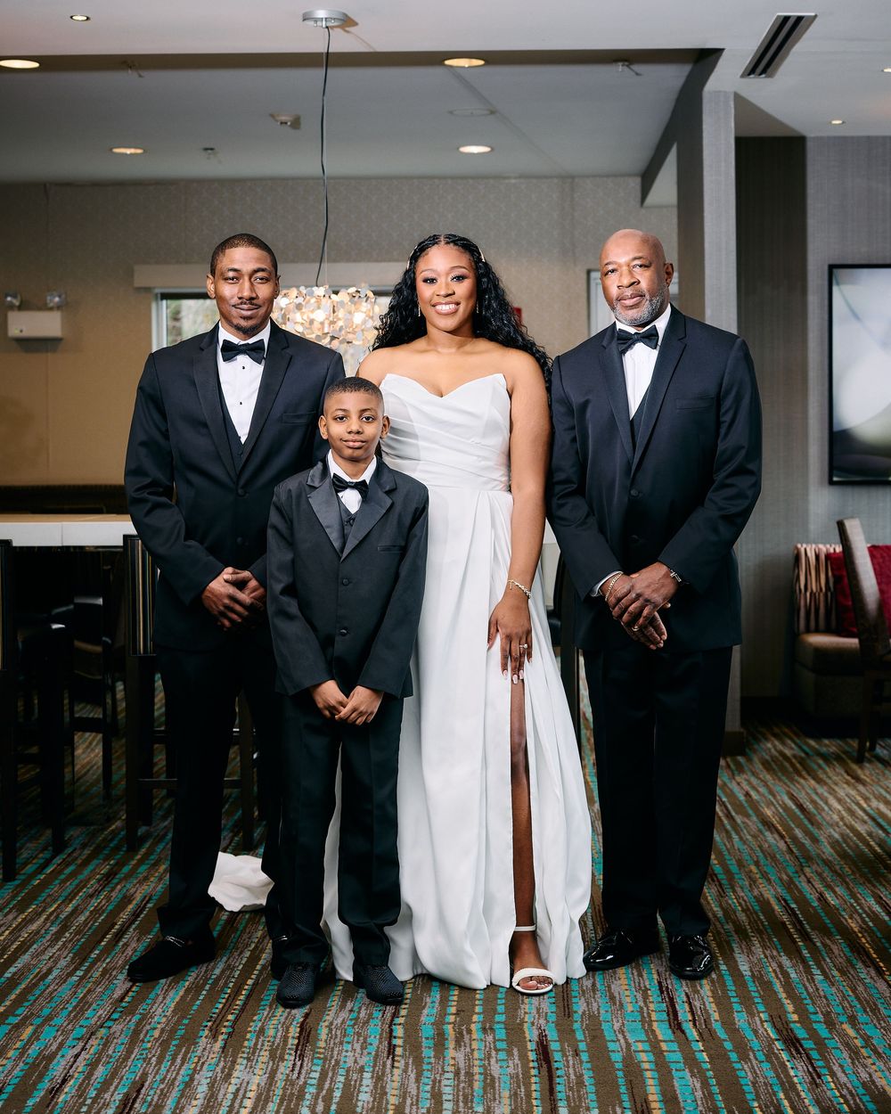 A bride in a white gown poses with three family members in formal attire at a wedding venue.