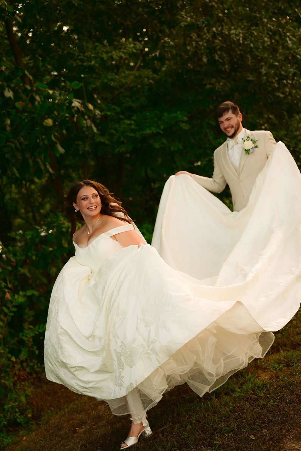 A flowing white wedding dress billows in the wind as someone walks through a garden setting at dusk.