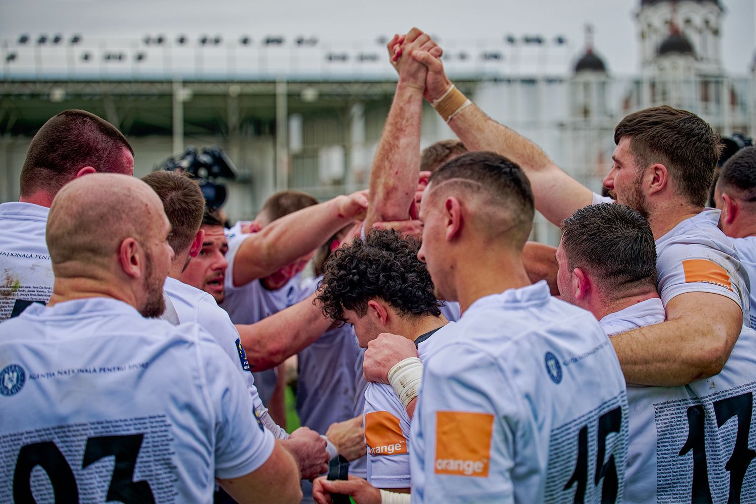 Rugby team celebrates victory with a group huddle on the field.
