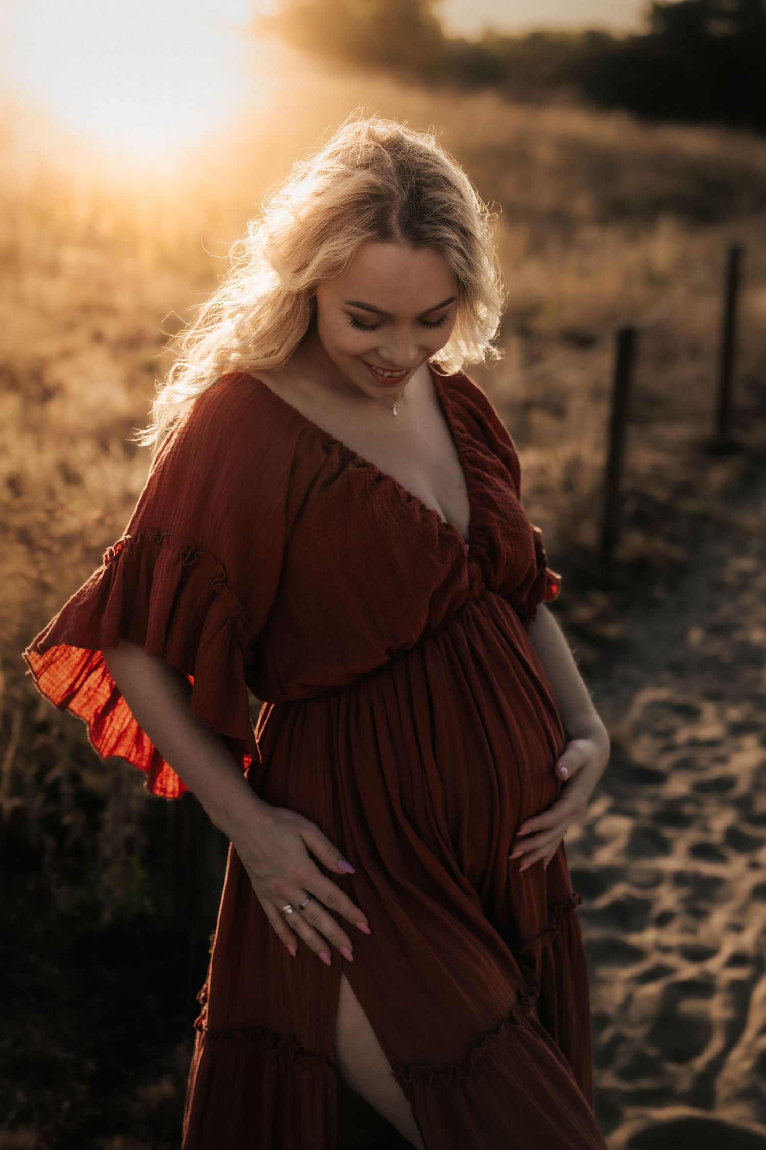 A flowing rust-colored dress catches the sunset light as someone poses on a sandy path.