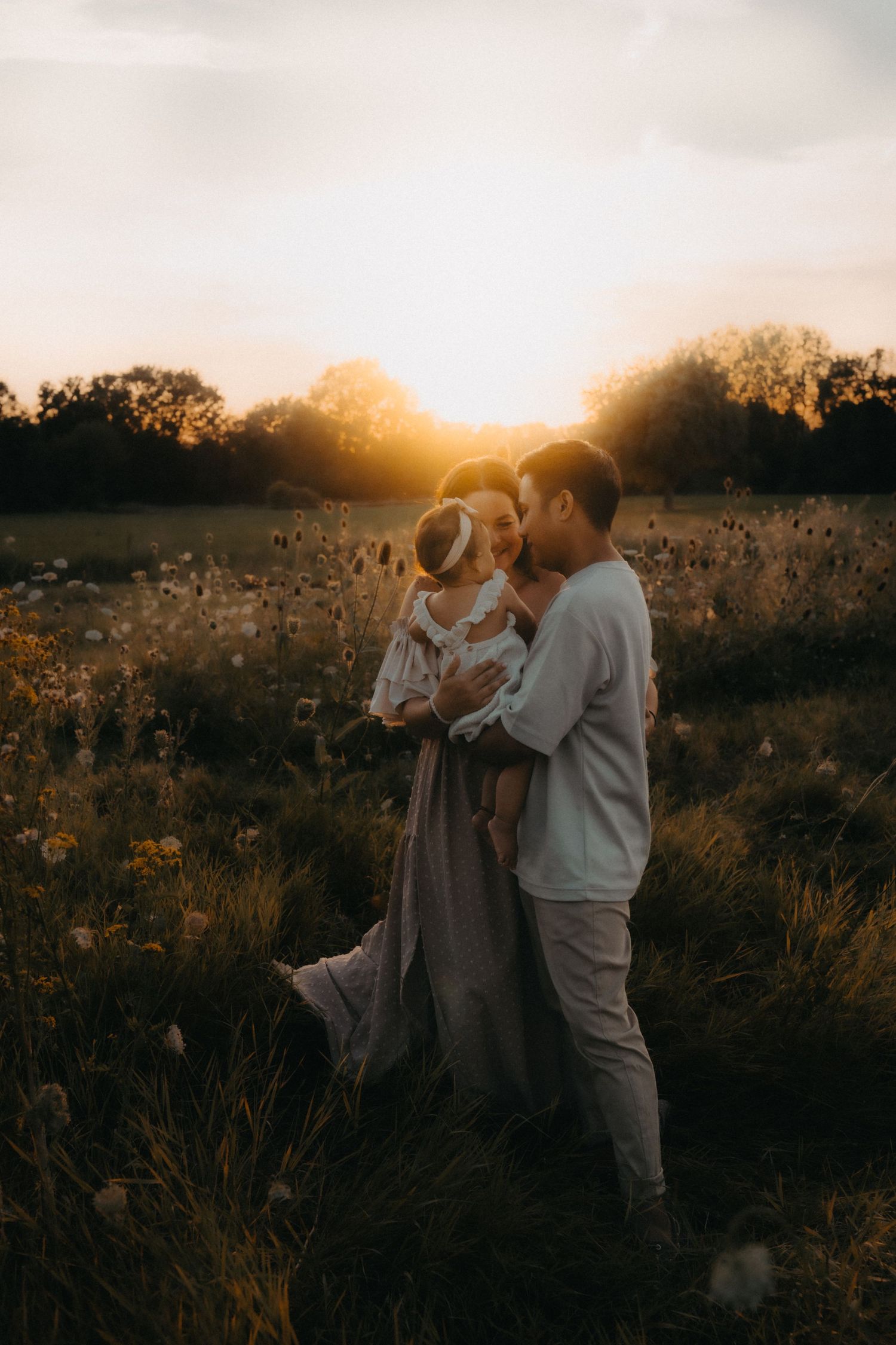 A romantic sunset scene with a couple and child in a wildflower field.