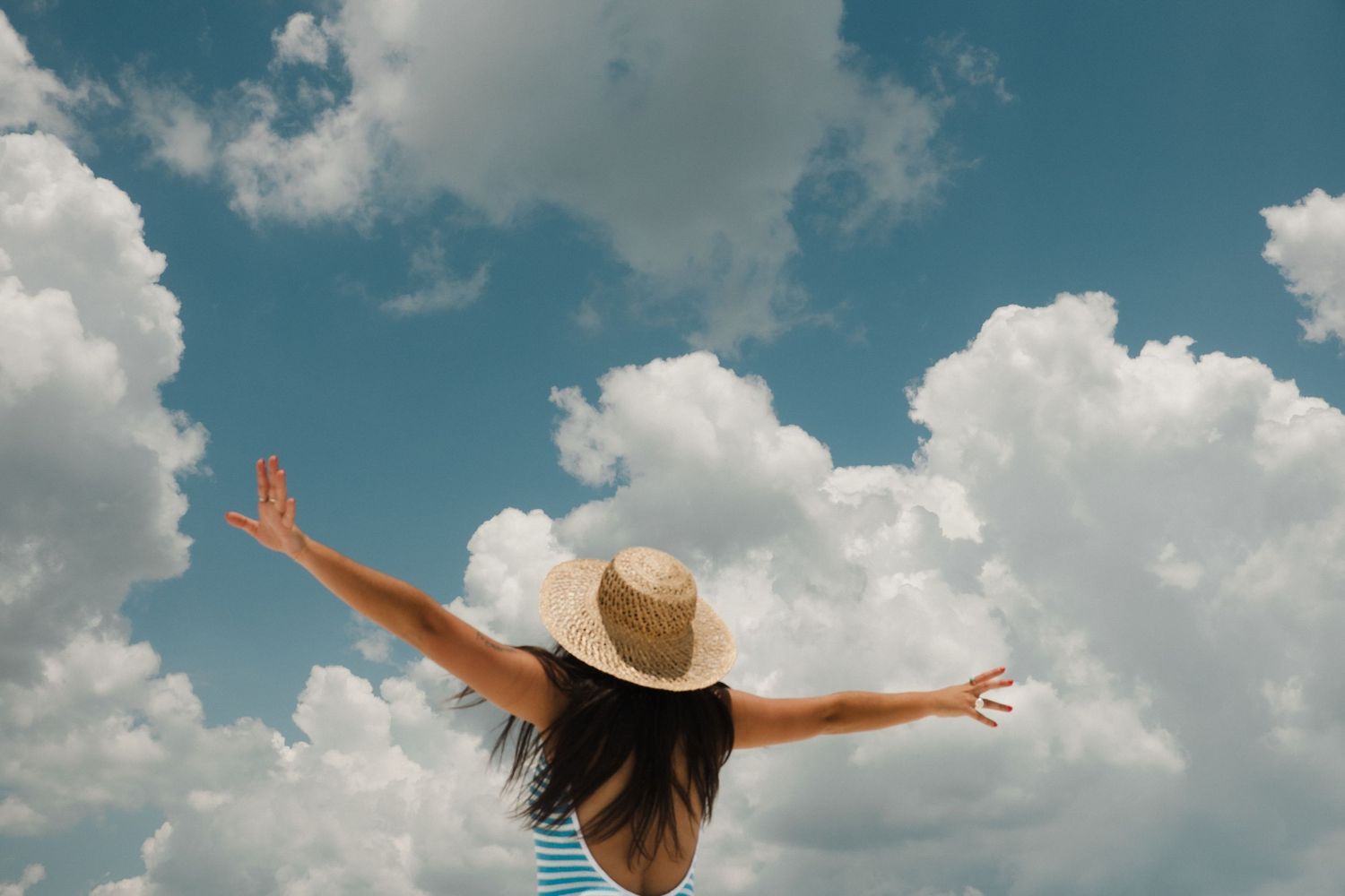 Person with outstretched arms against blue sky with fluffy white clouds.