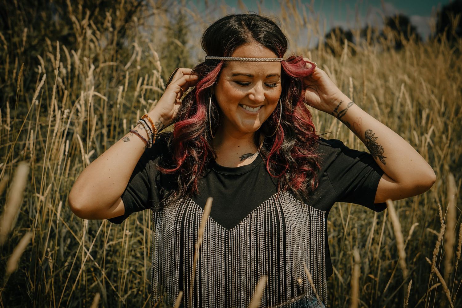 Woman adjusting headband in tall grass field during golden hour.