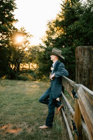 A husband poses for the groom portraits on his wedding day against a fence at Rustic Rose Barn in Guthrie, Oklahoma.