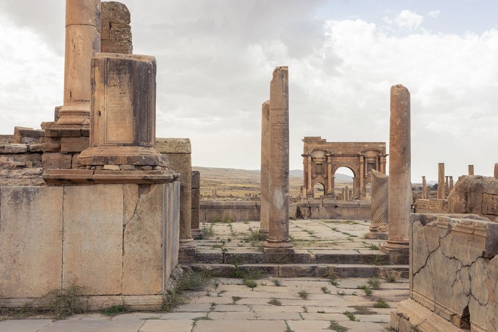 Panoramic view of ancient Roman ruins with columns and stone structures against a cloudy sky.
