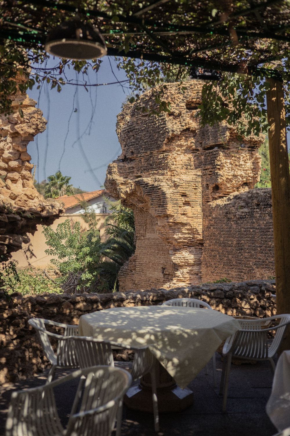 Stone wall ruins with outdoor dining tables and chairs set up in dappled sunlight.
