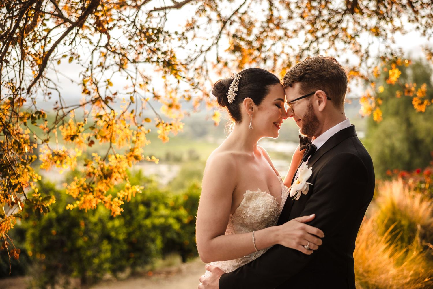 A tender moment between newlyweds during golden hour with autumn foliage in the background.