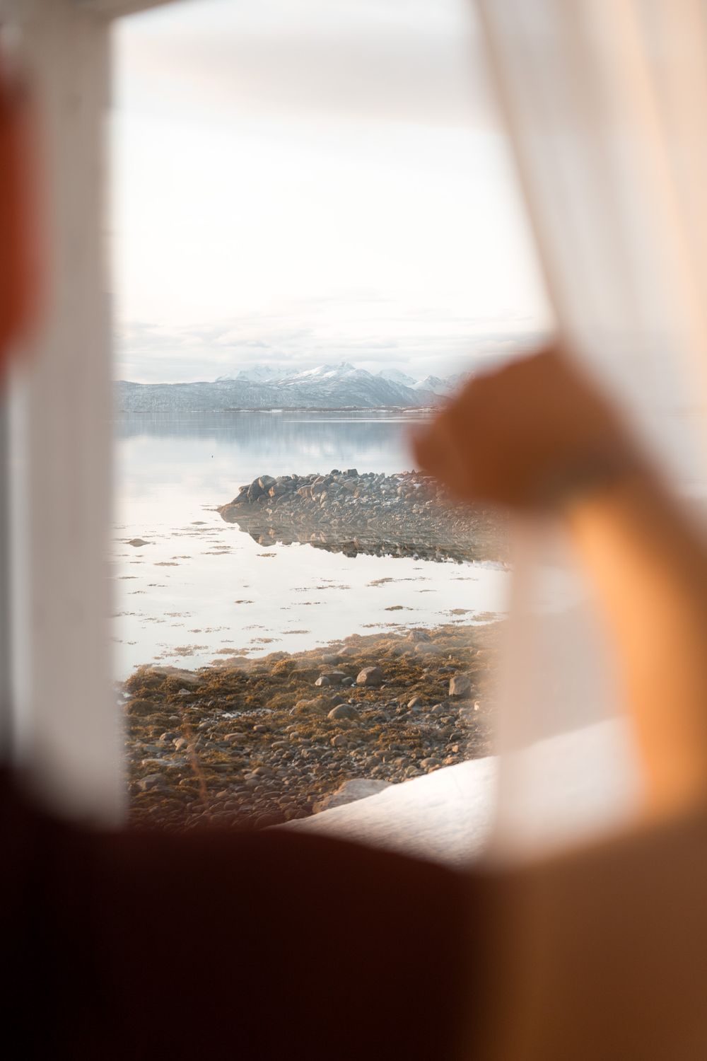 personne dans un hôtel de senja en norvège qui regarde par la fenêtre le fjord glacé