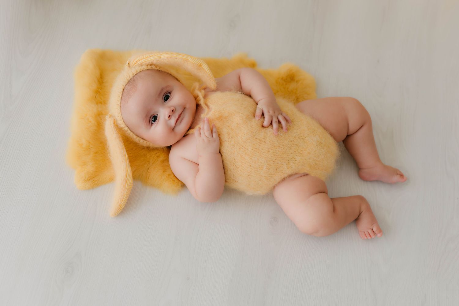 Bebé niña en una manta de pelo suave y vestida de conejita en tonos amarillos en una sesión fotográfica profesional.