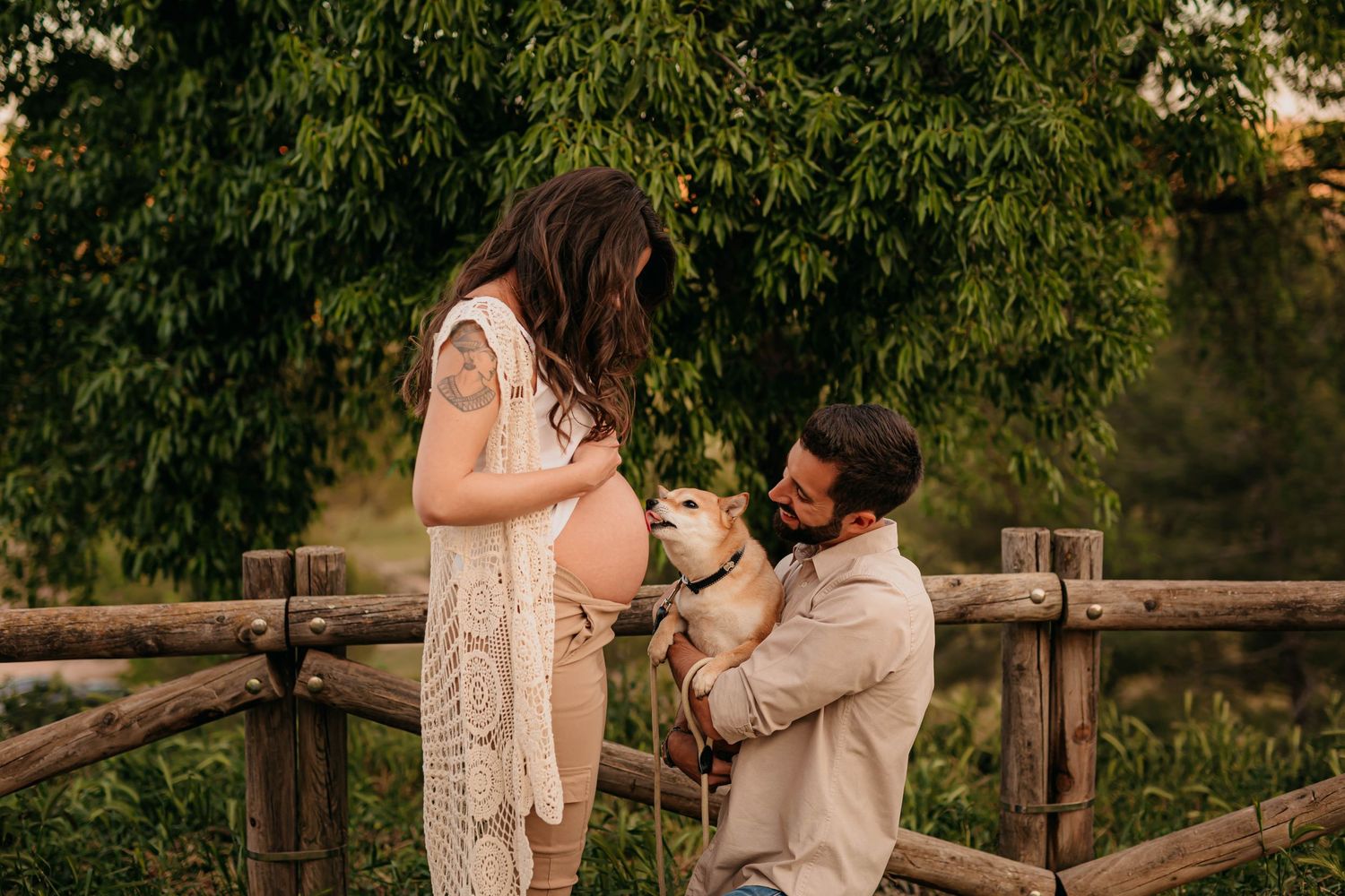 Fotografia de embarazo en exteriores donde la mascota de la familia lame la barriga de la futura mama