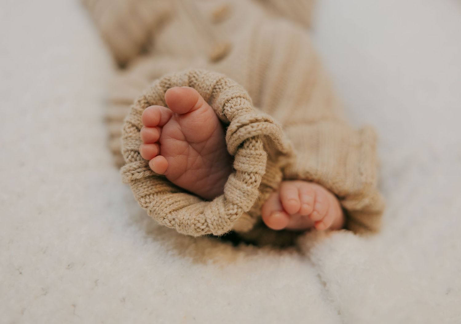 Tiny baby feet wrapped in a cozy knit blanket against a soft cream background.