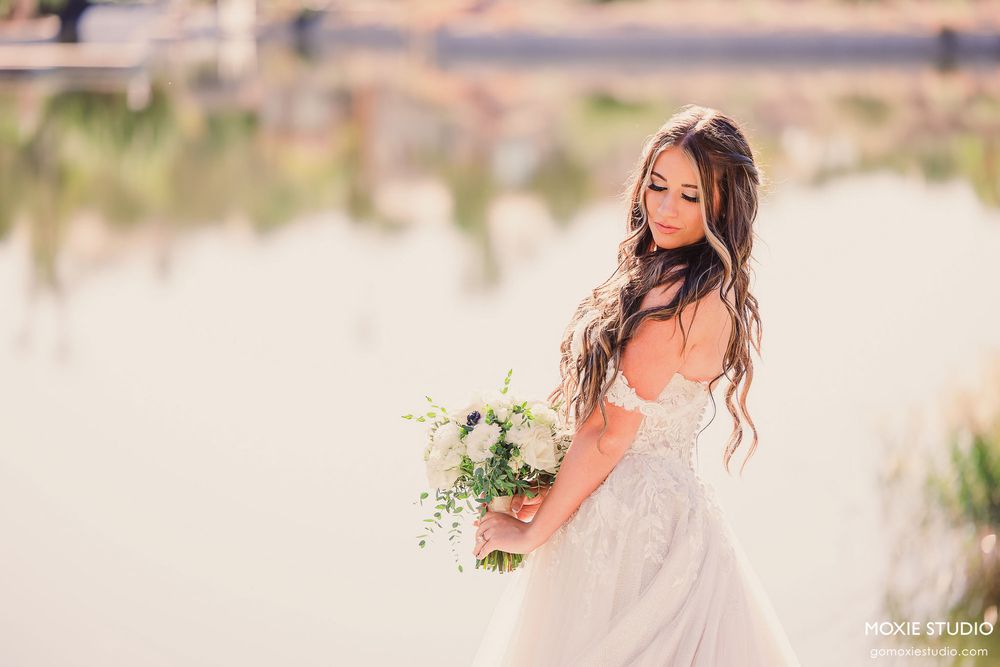 A bride in a flowing white dress poses in a sunlit desert landscape with mountains in the background.