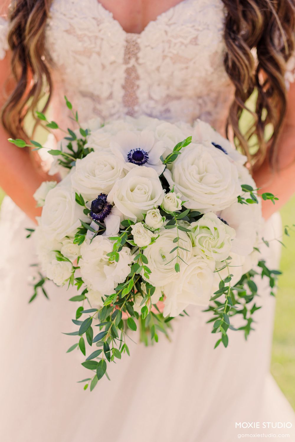 A delicate white bridal bouquet with navy blue accents and cascading greenery against a soft blush background.