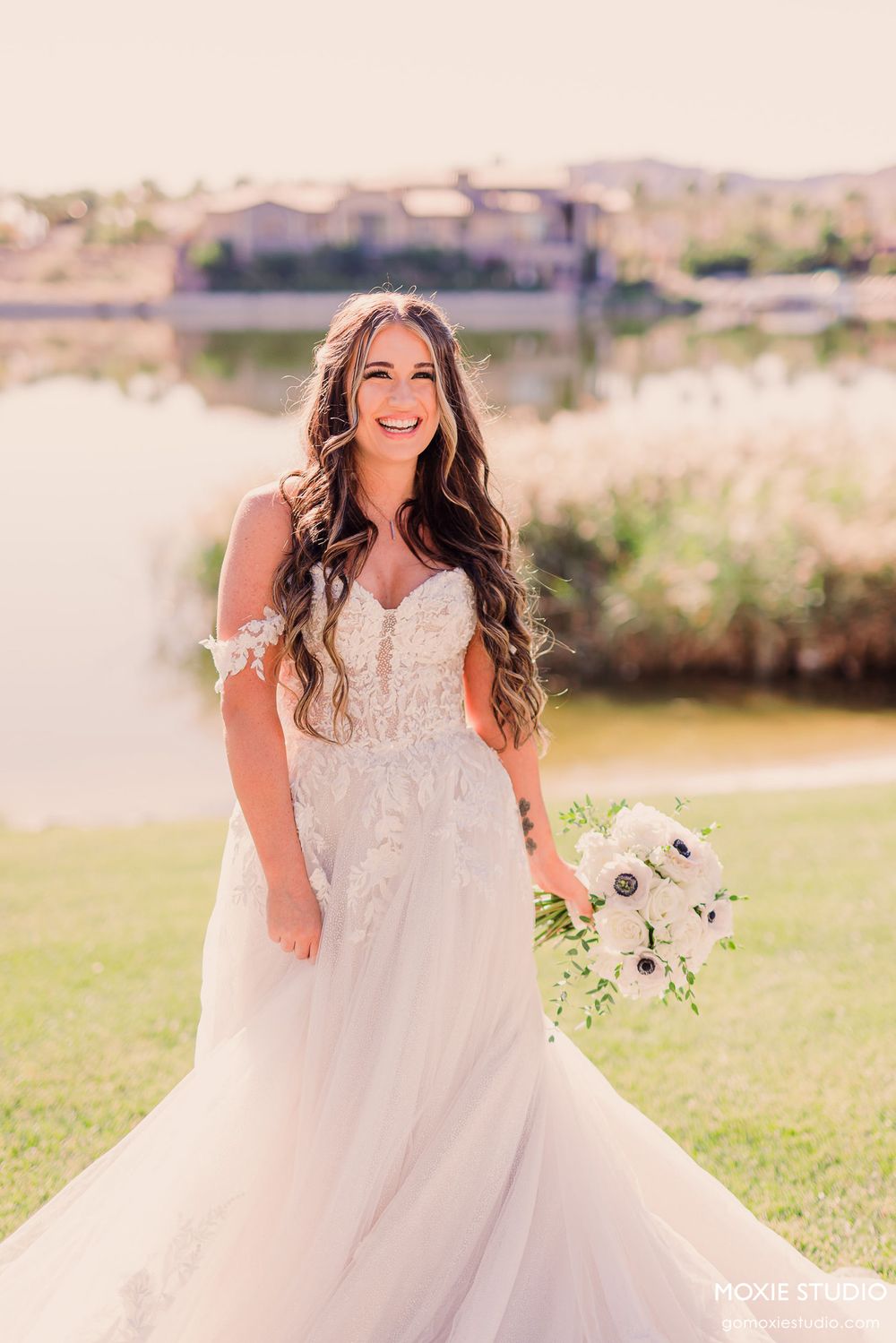 A joyful bride twirls in her lace wedding dress on a grassy lawn during a sunny outdoor photo session.