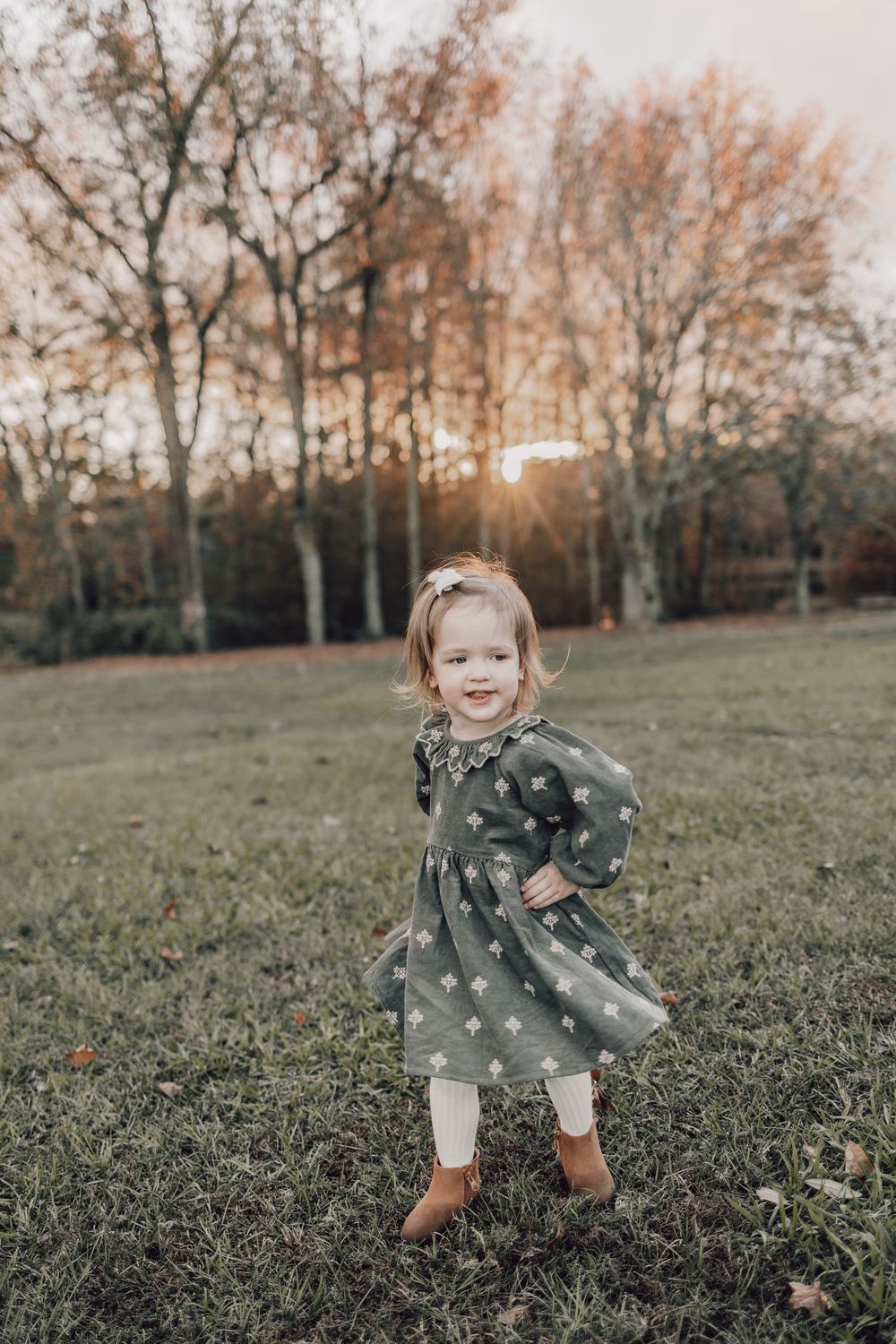 A small child in a polka dot dress runs and plays joyfully on a grassy hill during golden hour.