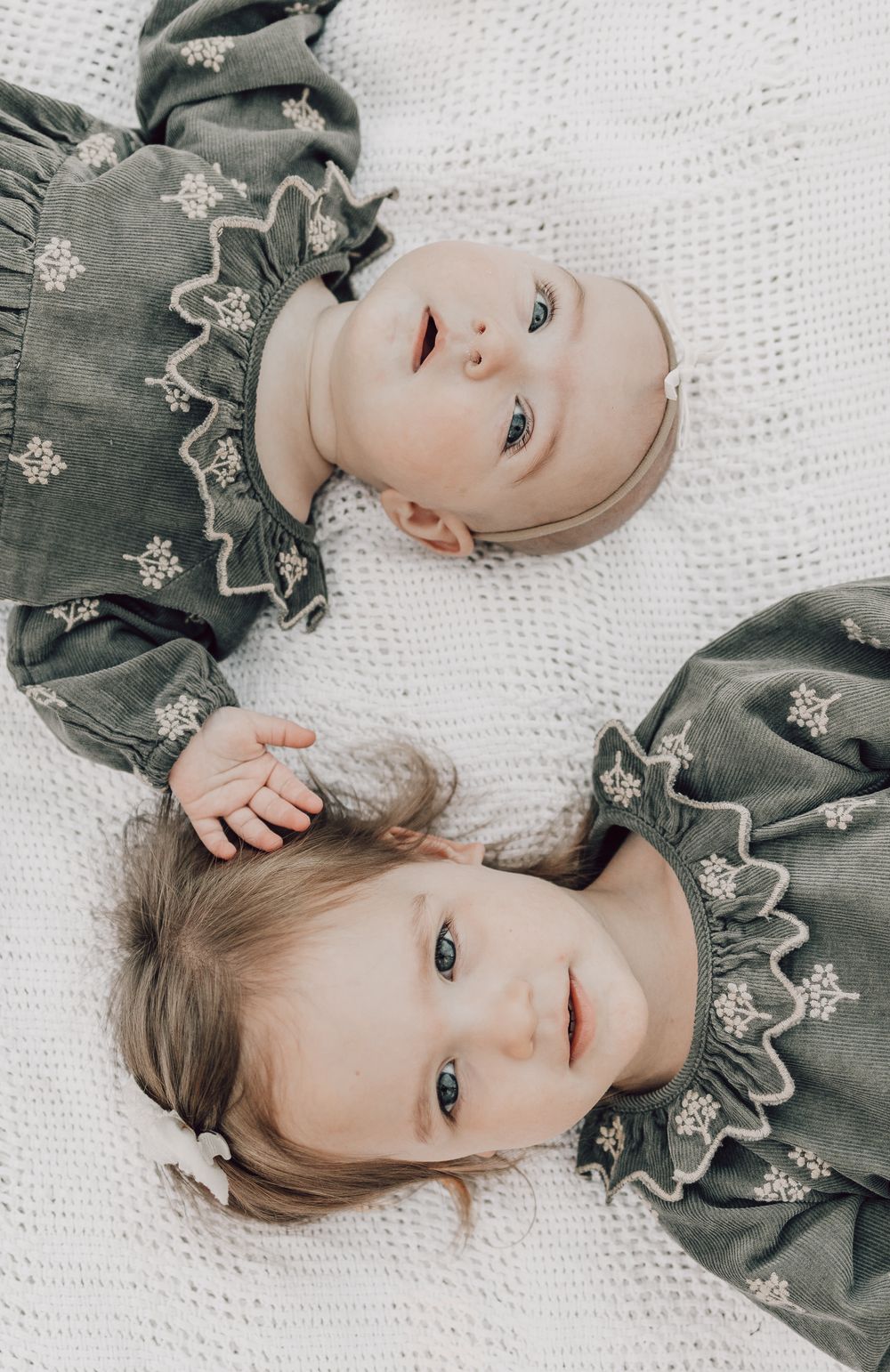 Baby in gray floral dress lying on white knit blanket smiling and looking at camera.