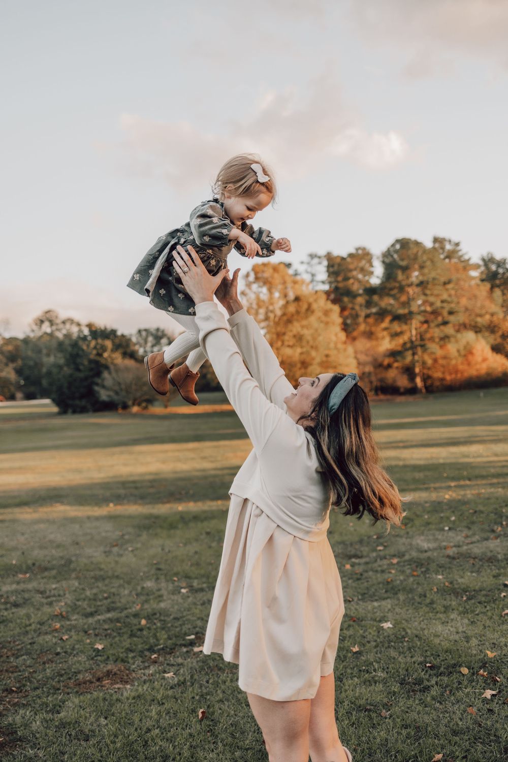 A joyful outdoor autumn photoshoot in a grassy field with warm golden lighting and fall foliage in the background.