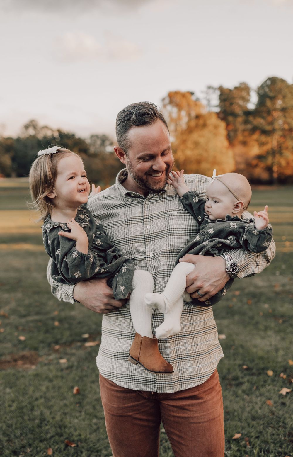 Joyful family moment outdoors with parent holding two children against fall scenery.