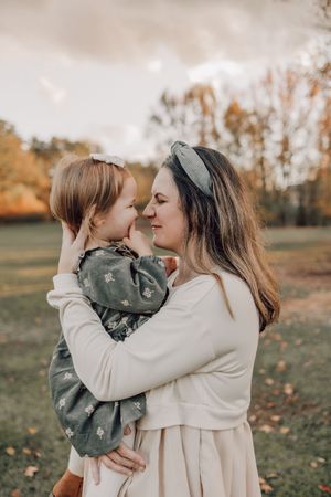 Tender moment between parent and child in autumn field wearing neutral tones.